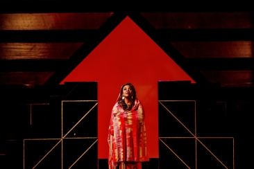 Aida stojąca na tle piramidy w kształcie czerwonej strzałki